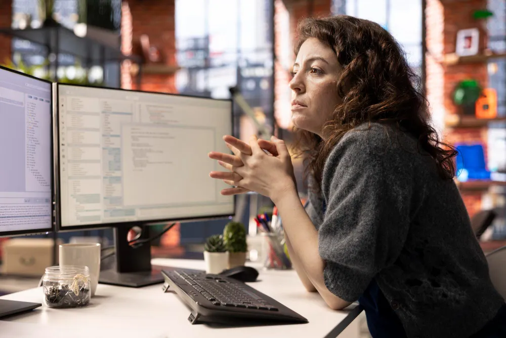 A writer editing a document on a laptop at a wooden desk with a notebook beside it