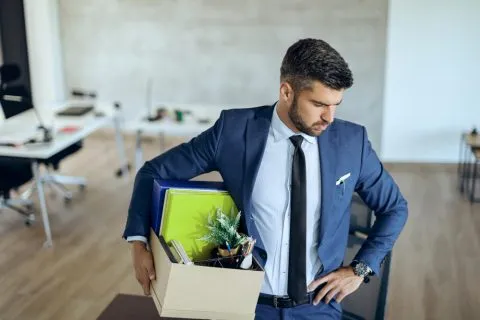 Employees carrying personal belongings outside a modern office building, illustrating the 2025 tech layoffs.