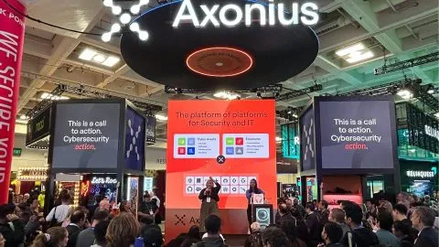 Axonius-branded cybersecurity office with employees working at computer monitors, illustrating Axonius layoffs 2025.