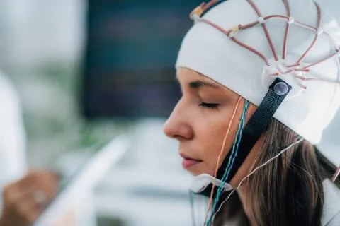 A person wearing a mixed reality headset with a curved glass front and white headband, photographed against a white background
