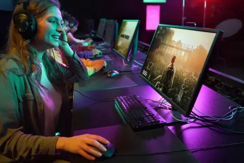 A person playing a streamed video game on a thin laptop with a wireless controller at a kitchen table