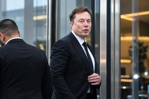 Elon Musk in a dark suit standing in a modern corporate lobby, illustrating the Elon Musk Skydance investment