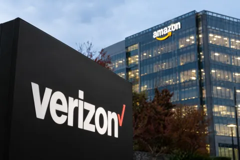 Verizon and Amazon corporate signage in a realistic editorial illustration of the Verizon Amazon AWS deal worth more than $2 billion.