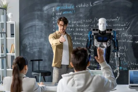 Why students should learn AI: A teacher explains programming beside a humanoid robot while students participate in a classroom lesson.