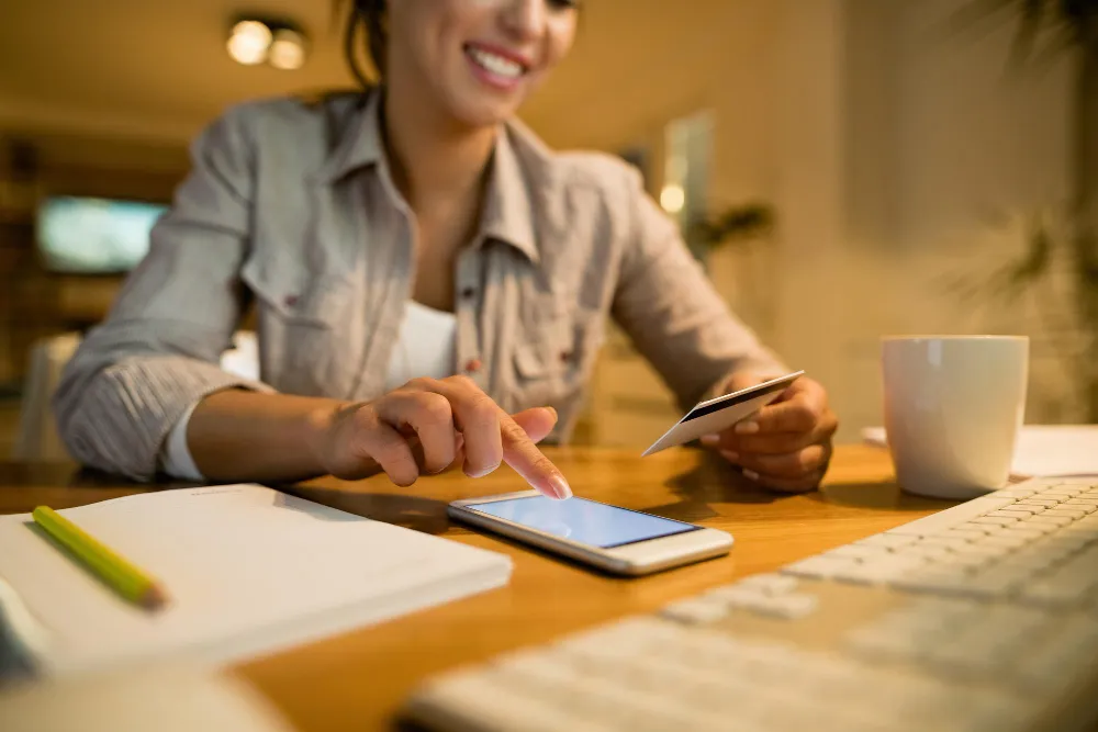A person holding a smartphone open to a checking account balance screen at a cafe table