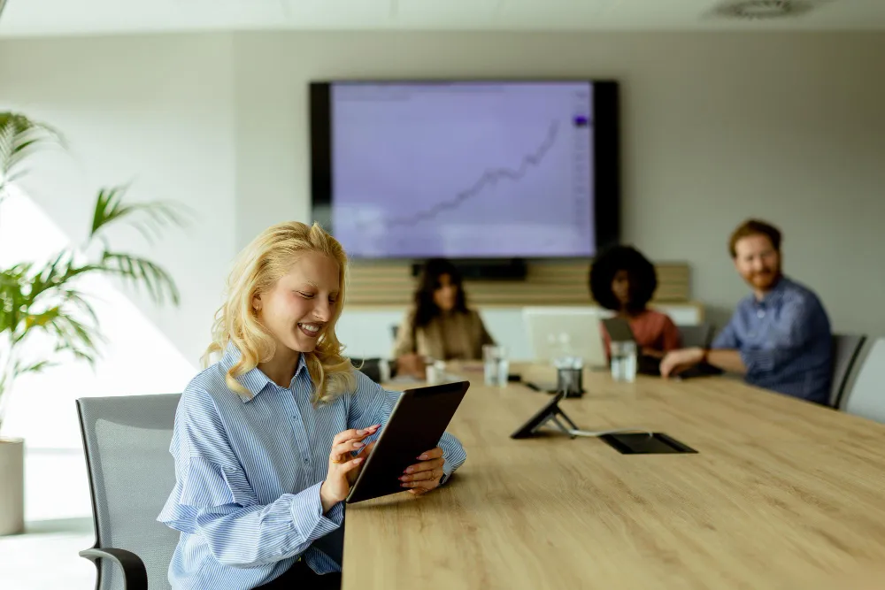 Smart meeting room technology in a modern conference room with employees participating in a hybrid video meeting using a large display and connected conferencing equipment.